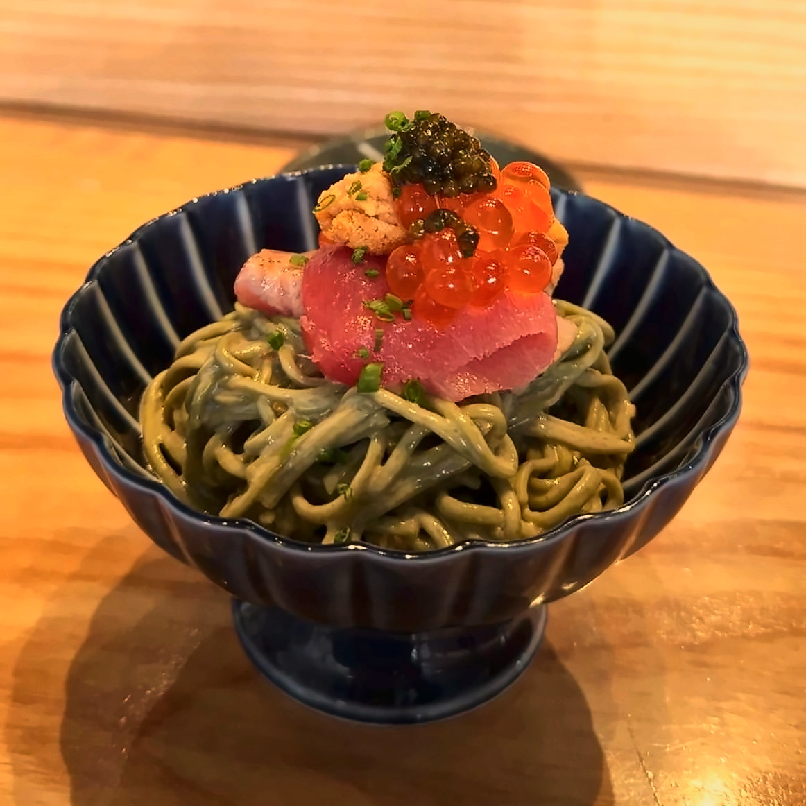 Green soba noodles topped with tuna, salmon roe and caviar in a fluted blue bowl.