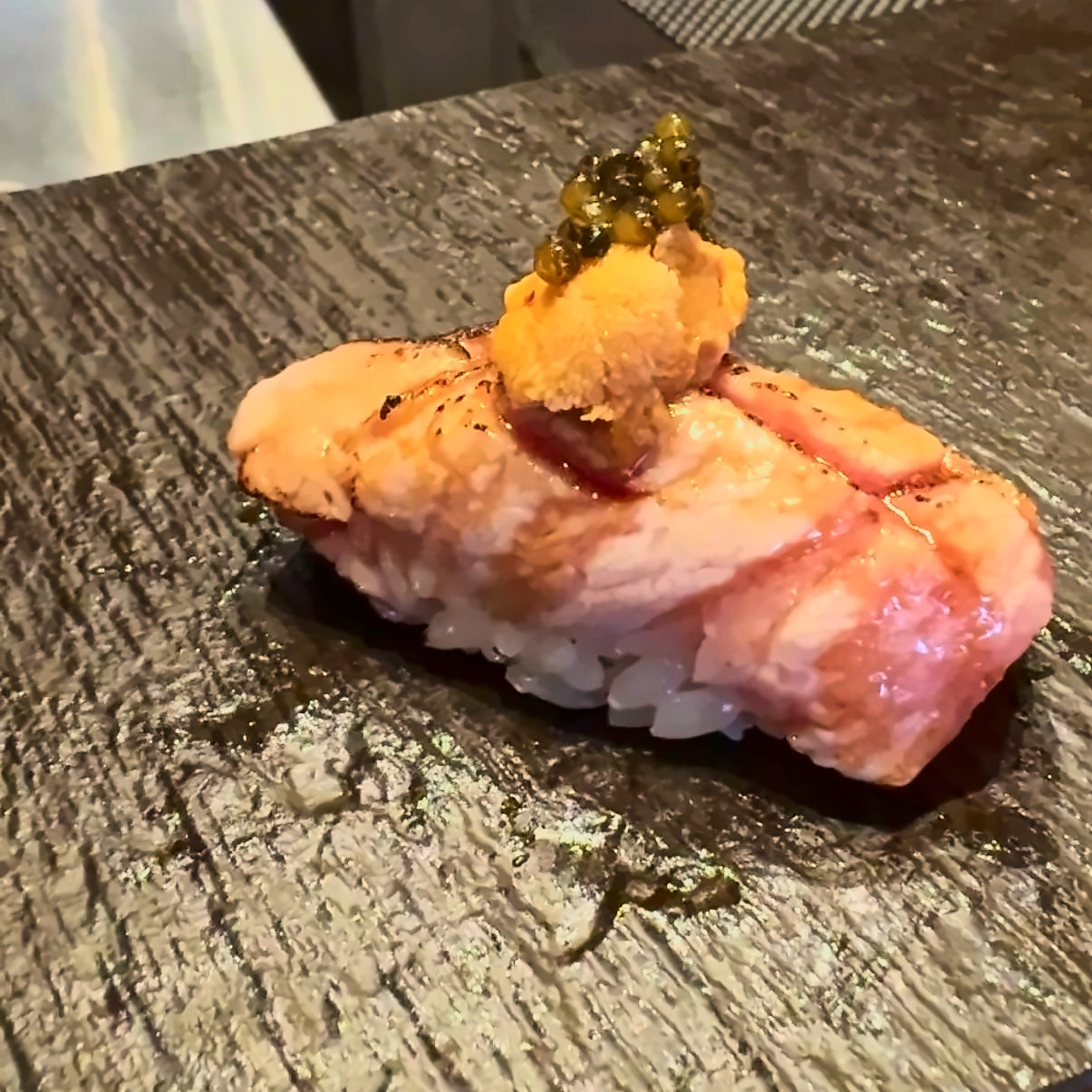 Seared nigiri topped with sea urchin and caviar on a dark slate plate.
