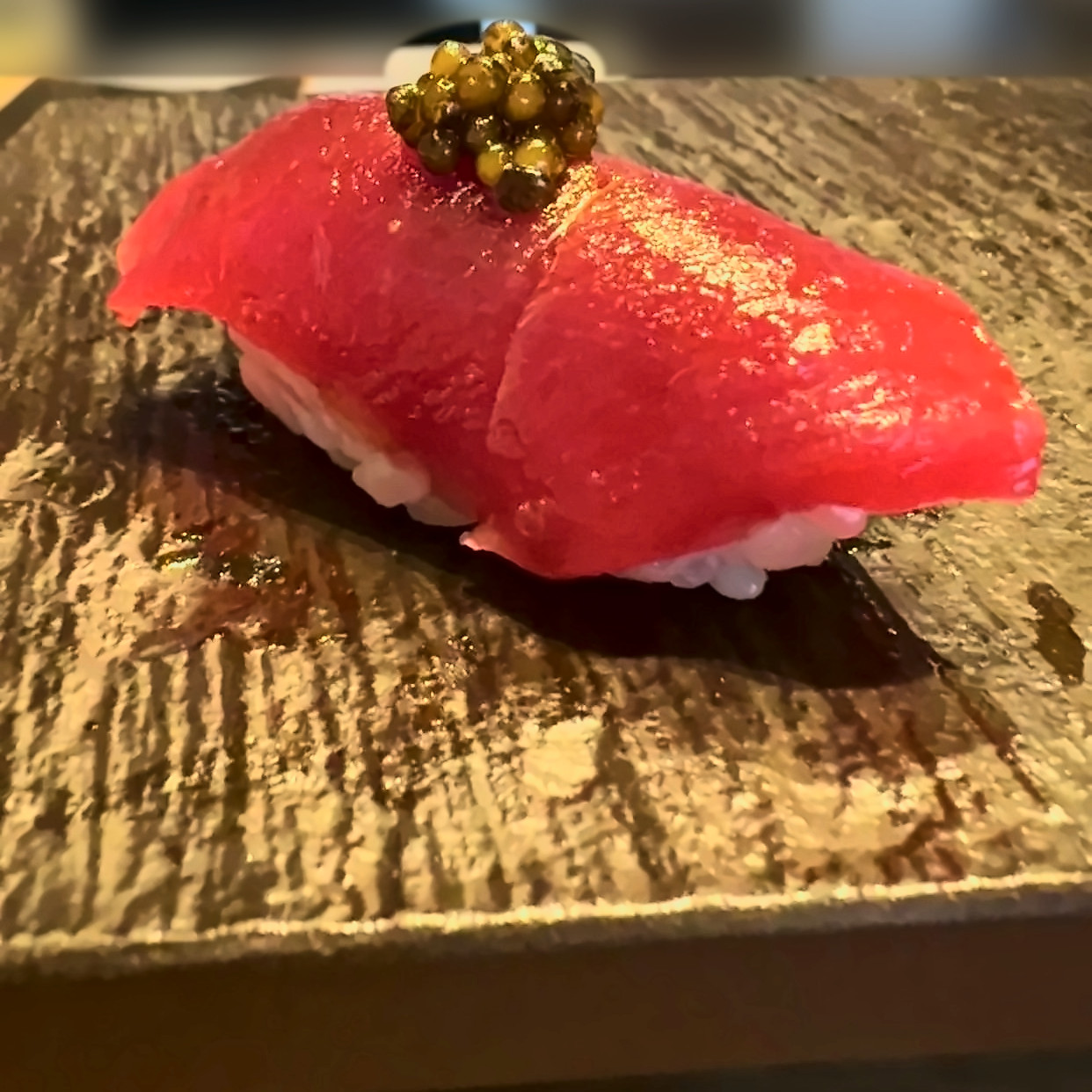 Tuna nigiri topped with caviar on a dark slate plate.