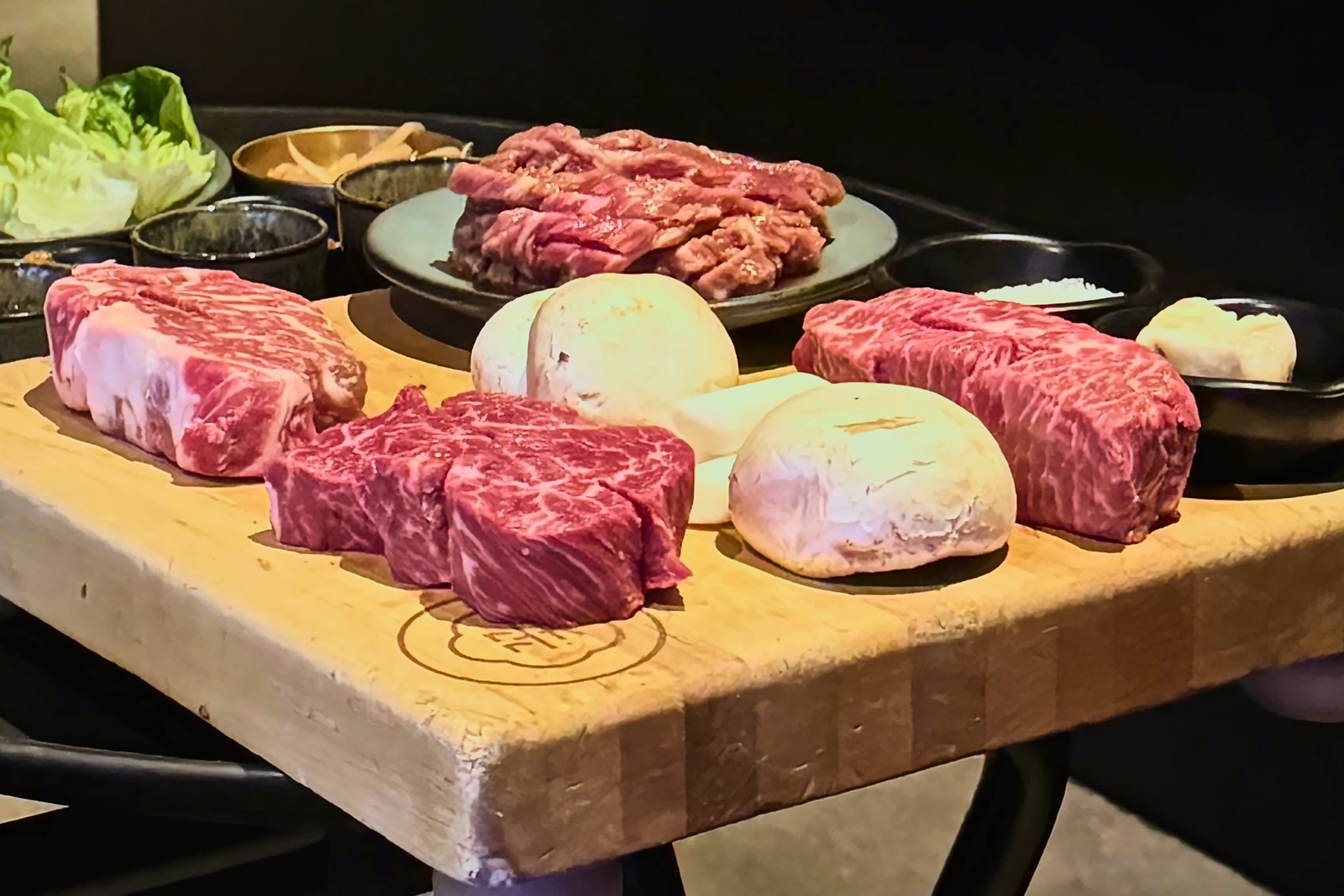 Raw marbled beef cuts and mushrooms on a wooden butcher's board.